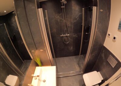 Badezimmer mit schwarzen Steinfliesen, Toilette, Waschbecken und Dusche